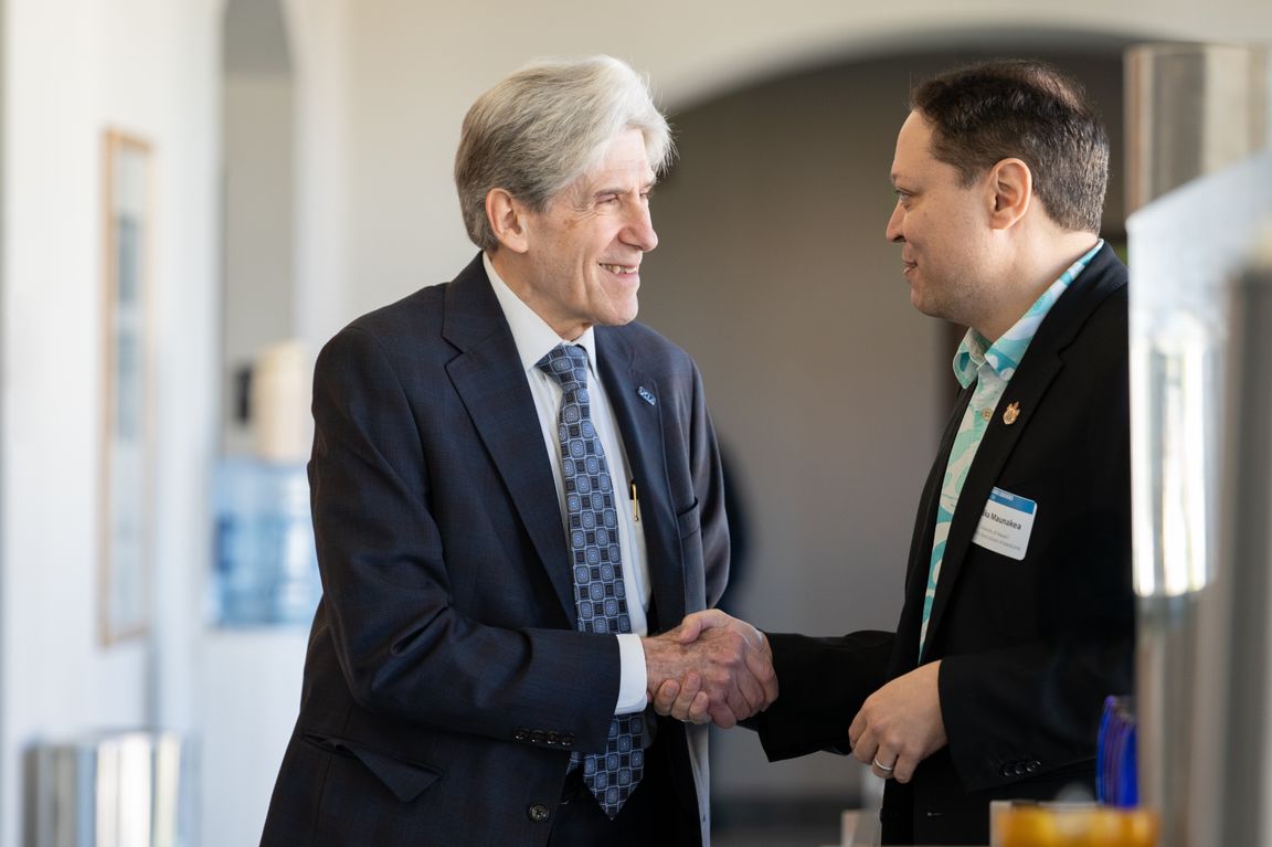UCLA Chancellor Julio Frenk (left) shakes hands with University of Hawaii epigeneticist Alika Maunakea at an indoor event focused on lessons from the 2023 Lahaina wildfire.