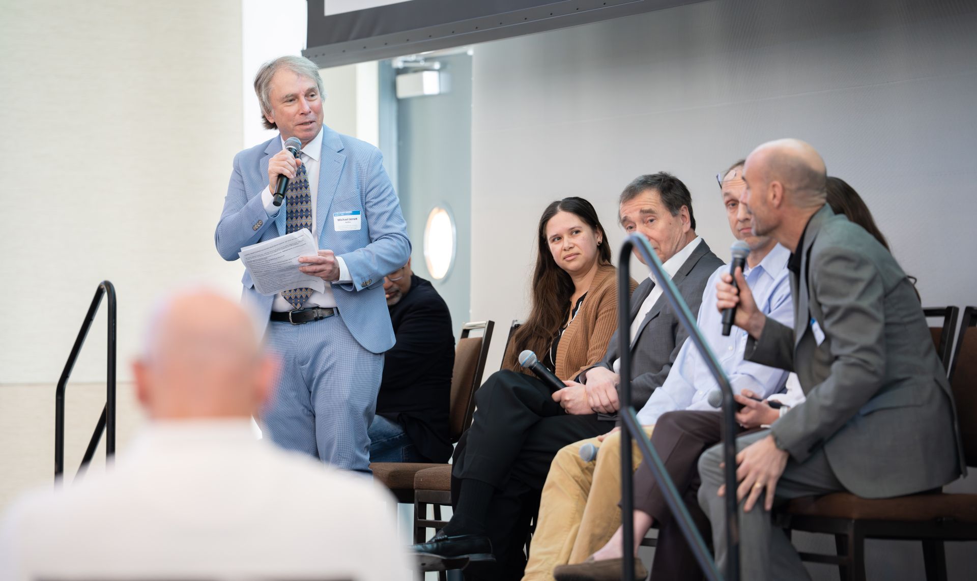 UCLA's Michael Jerrett stands and speaks into a microphone in a light blue suit while four fellow panelists seated beside him listen during a research discussion on air-quality data challenges.