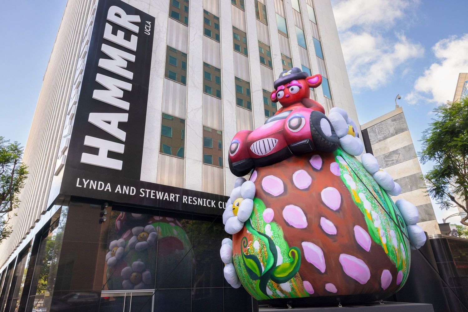 A large colorful sculpture of a whimsical figure atop a spotted mushroom displayed outside the Hammer Museum in Los Angeles.