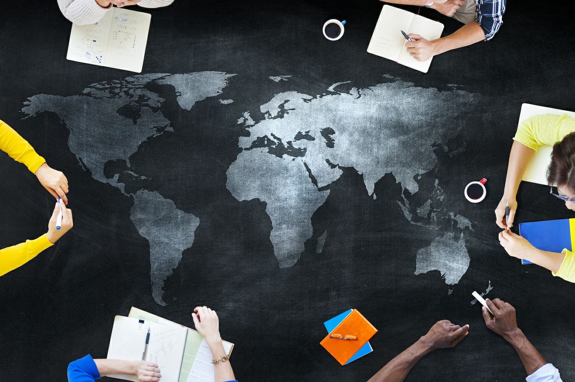 Map of the global surrounded by various people's hands holding or writing in notebooks