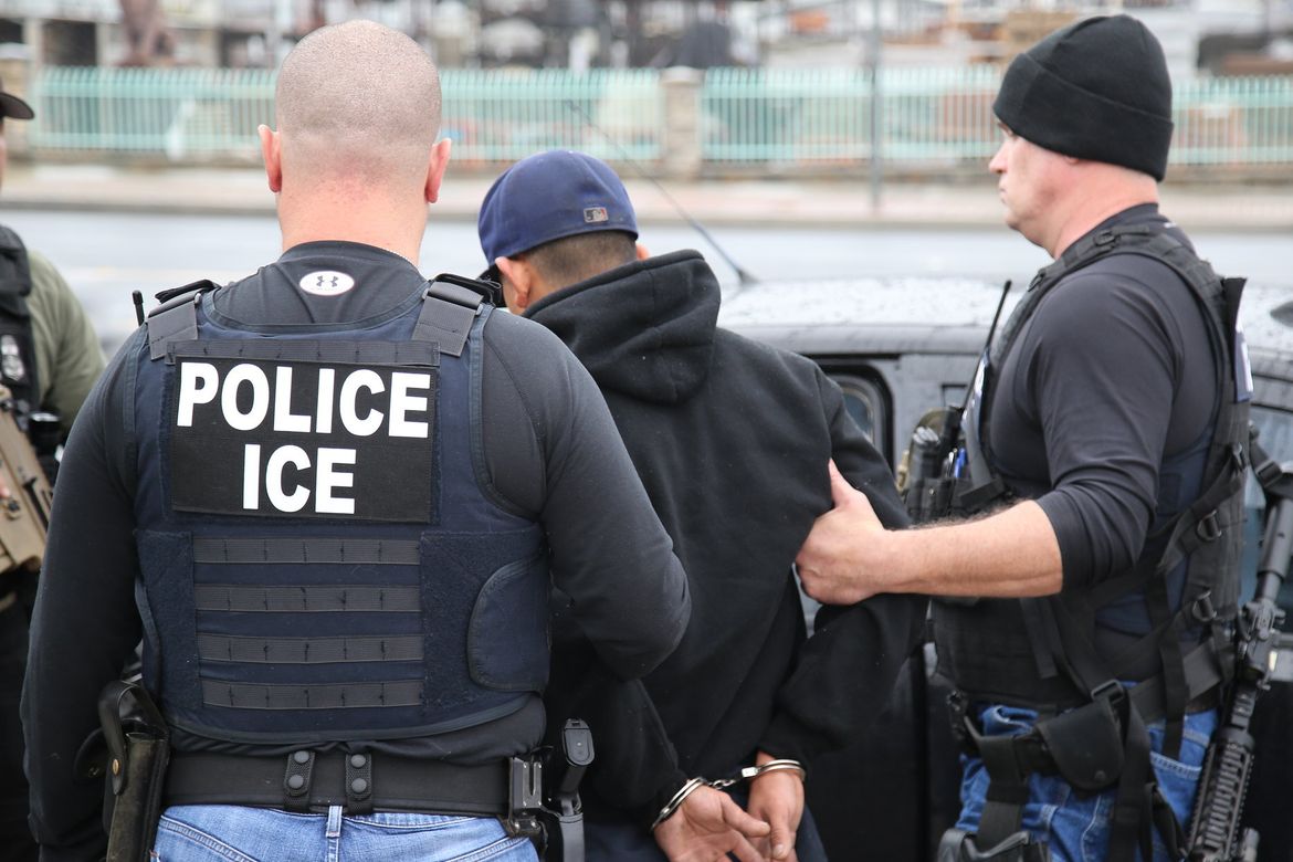 Dos agentes del Servicio de Inmigración y Control de Aduanas esposan a un hombre que lleva una sudadera con capucha negra