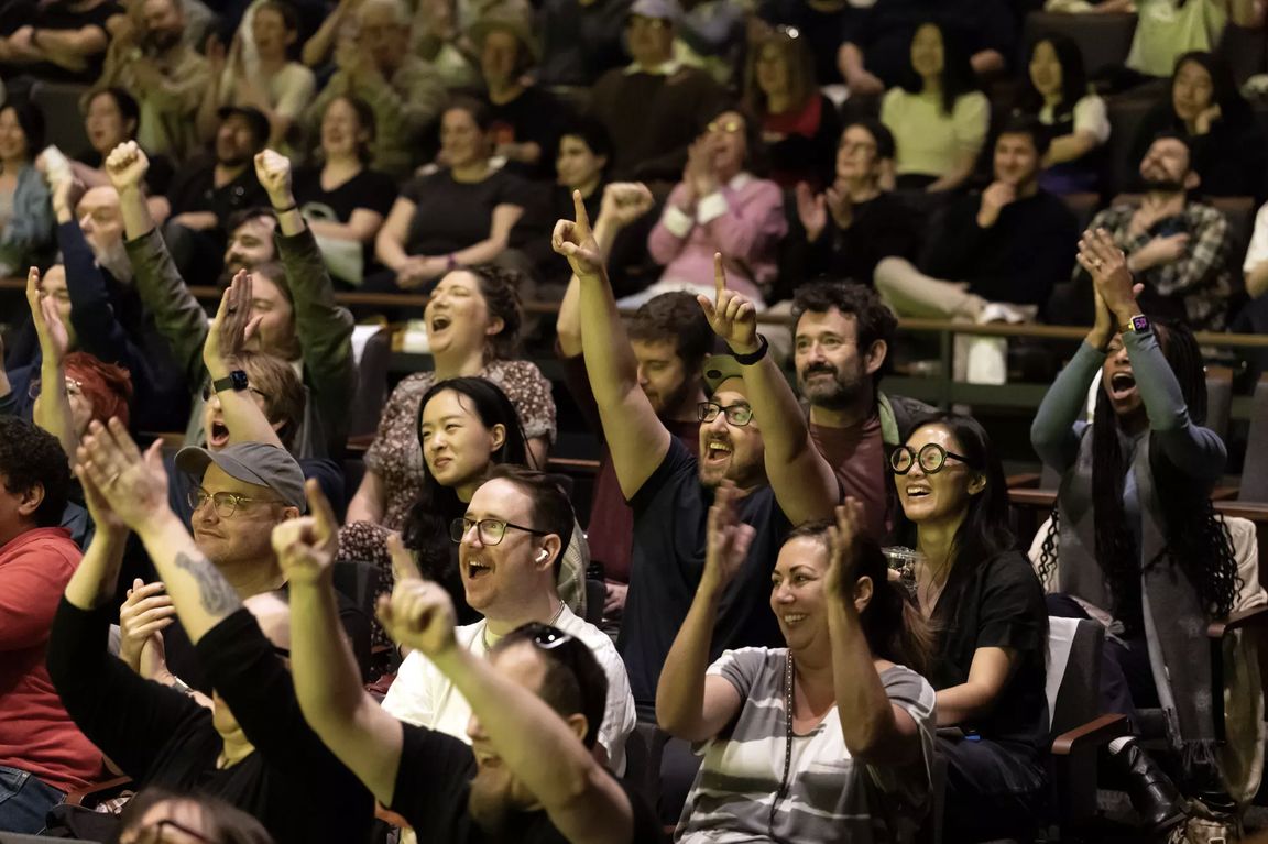 A diverse crowd of audience members cheering and raising their fists during an interactive video game marathon event.