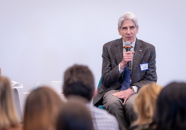 Chancellor Julio Frenk speaking into a microphone while seated before an audience at the Geffen Academy.