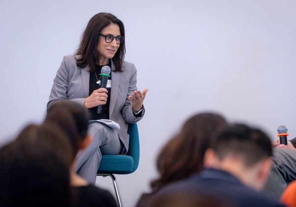 Christina Christie speaking into a microphone while seated before an audience at the Geffen Academy.