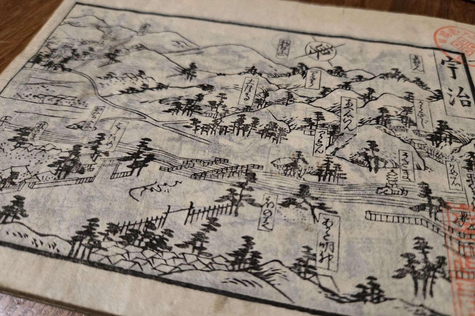 A historical Japanese woodblock-printed map showing mountains, trees, roads, and labeled landmarks with Japanese text, printed on aged paper with red seal stamps visible on the right edge.