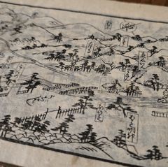 A historical Japanese woodblock-printed map showing mountains, trees, roads, and labeled landmarks with Japanese text, printed on aged paper with red seal stamps visible on the right edge.