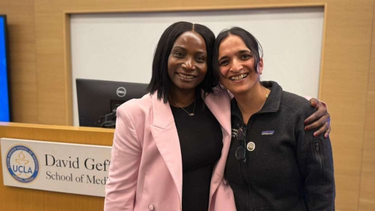 Two women smile with their arms around each other in front of a UCLA David Geffen School of Medicine podium sign.