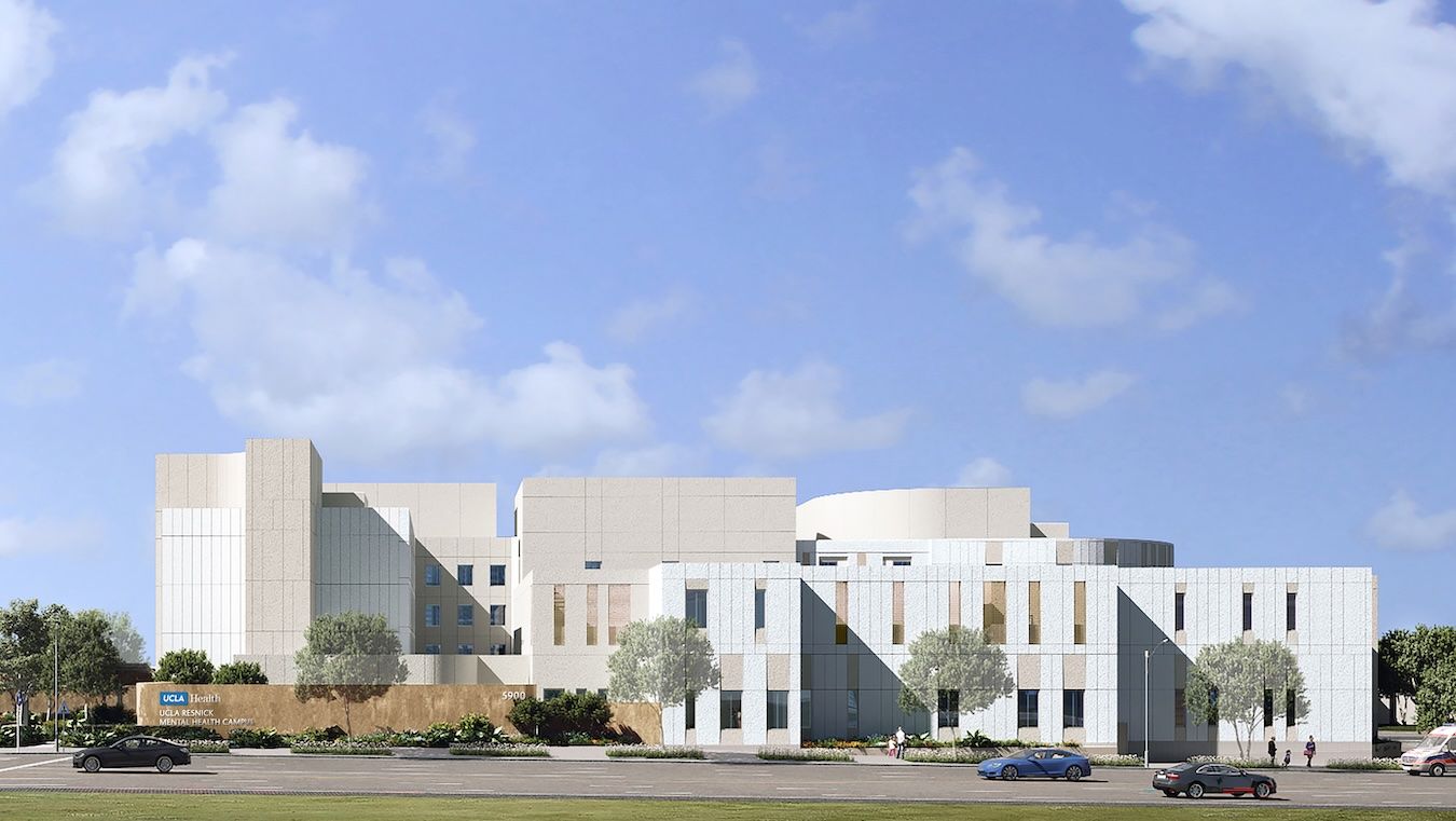 An architectural rendering of the proposed UCLA Health neuropsychiatric hospital and comprehensive mental health campus, showing a modern multi-story building with light-colored stone and glass facades surrounded by trees under a blue sky.