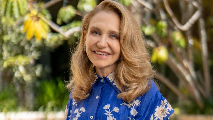 Felicia Marie Knaul smiles in a portrait photo wearing a blue floral blouse, with lush tropical greenery in the background.
