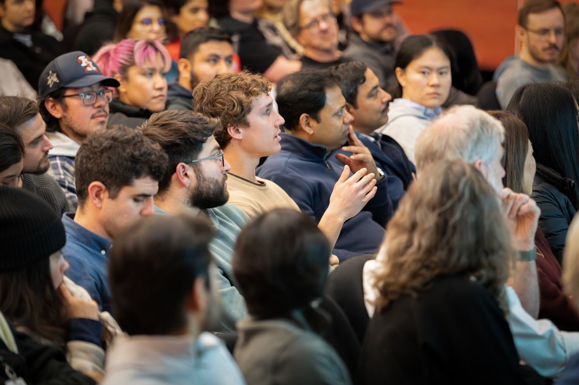 A diverse crowd of students and faculty listens attentively during a seminar in an auditorium.