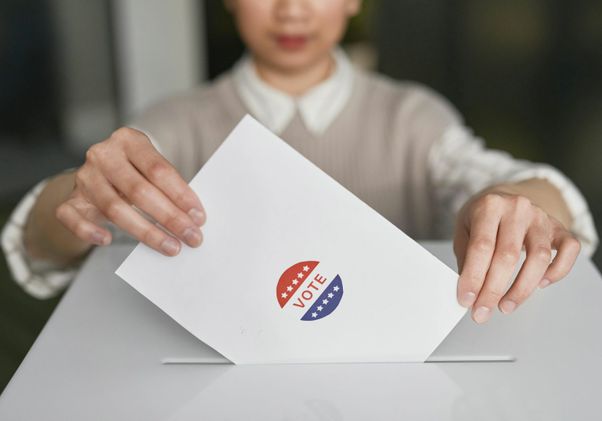 A person slides a ballot envelope marked with a red, white and blue 