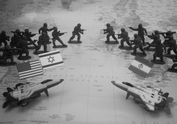 A black-and-white conceptual illustration shows two opposing groups of toy soldiers facing each other on a world map, with miniature flags of the United States and Israel on one side and Iran on the other, flanked by model fighter jets.