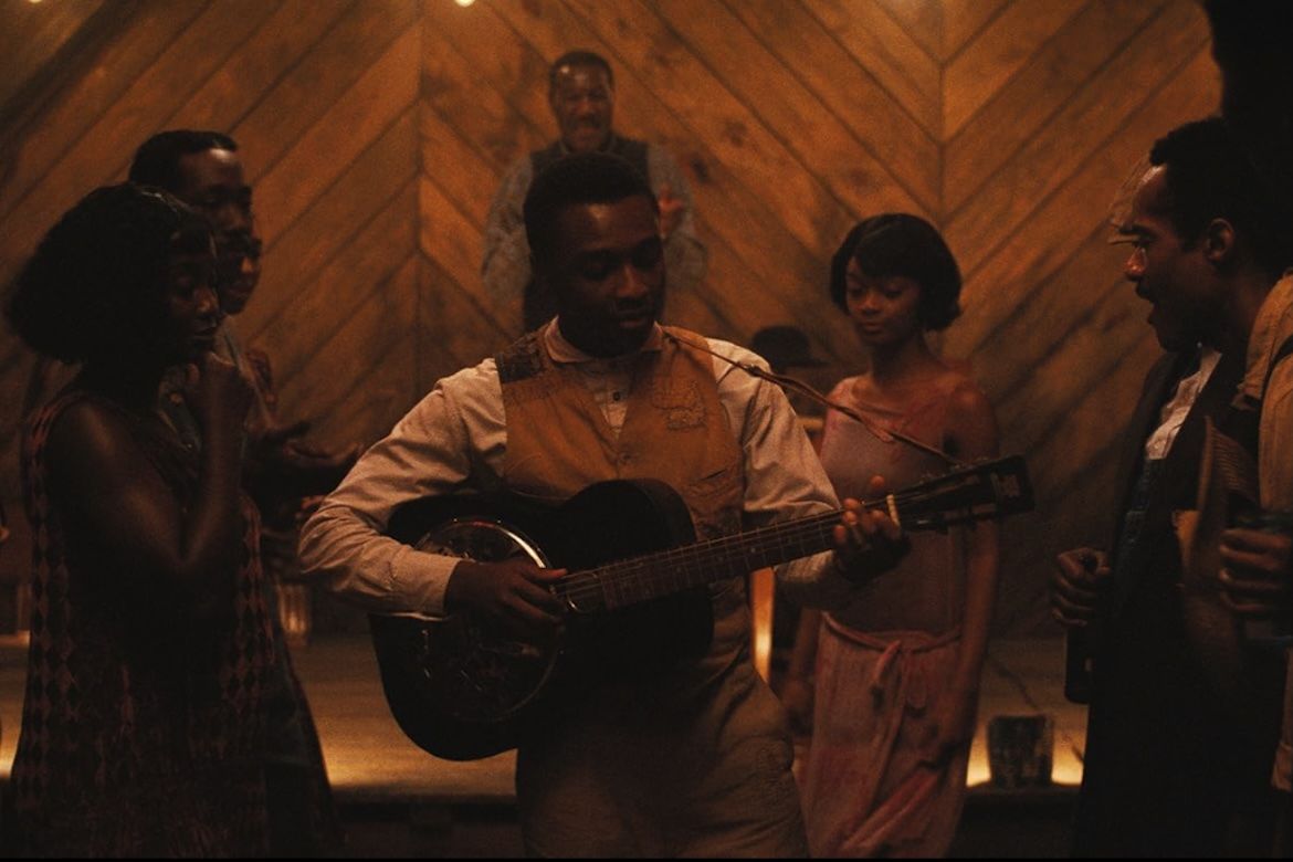 The character "Preacher Boy" Sammie plays acoustic guitar at a juke joint in a scene from the 2025 film "Sinners." 