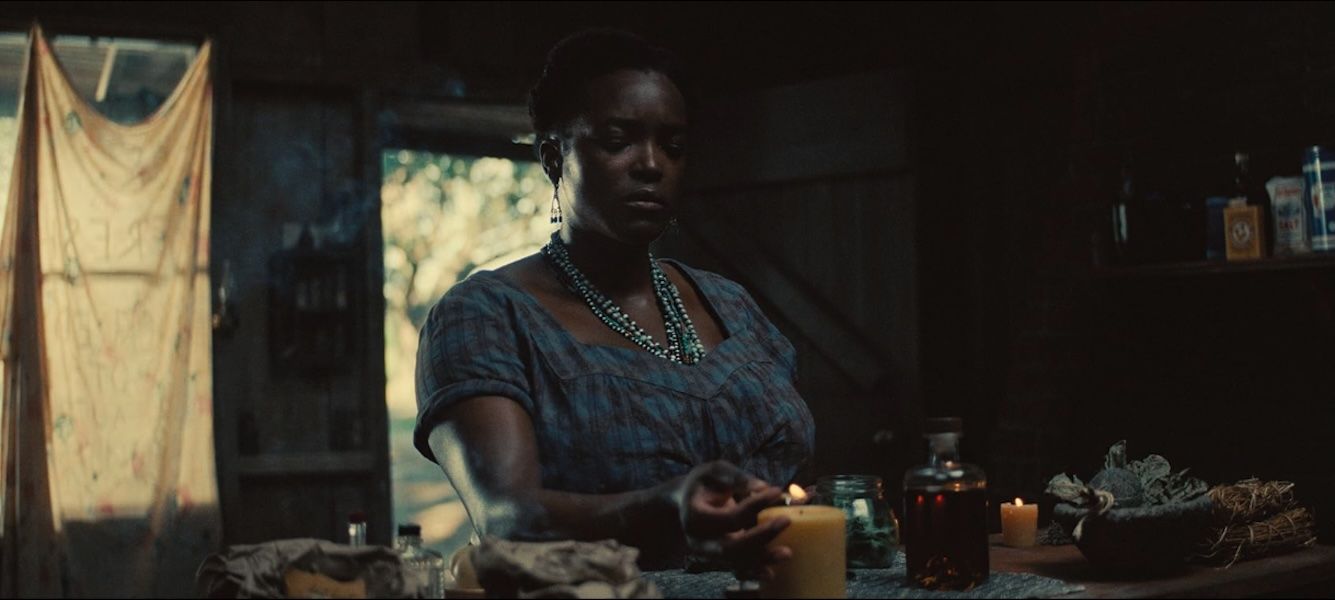 The character Annie stands at a table surrounded by candles and herbs while performing a hoodoo ritual in a scene from "Sinners."