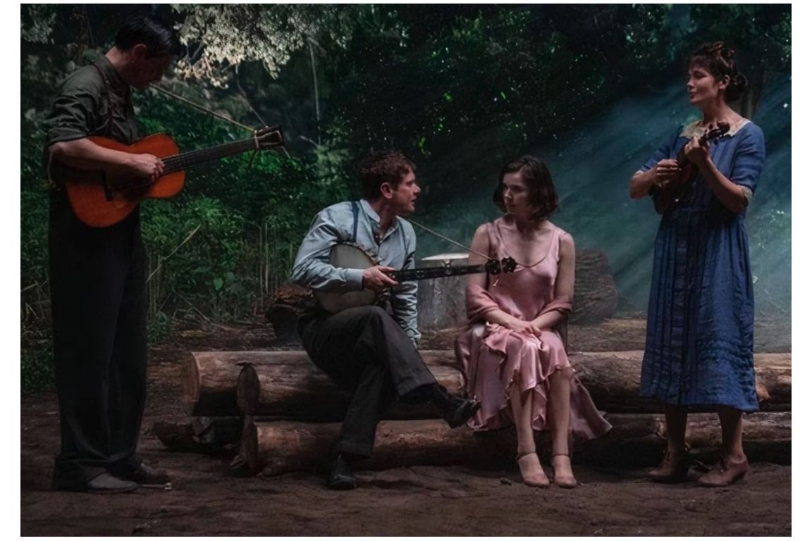 The vampire leader Remmick and his followers sit on a log playing instruments outdoors in a scene from "Sinners." 