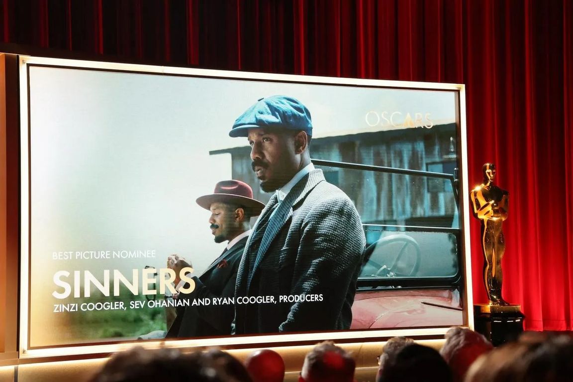 A large screen displaying the Oscars Best Picture nominee "Sinners," produced by Zinzi Coogler, Sev Ohanian, and Ryan Coogler, is shown on stage next to an Academy Award statuette against a red curtain backdrop.