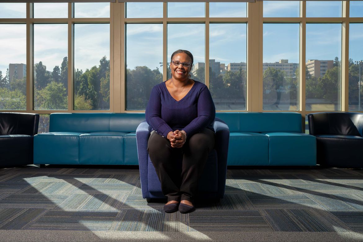 Nicole Presley, in blue shirt and black pants, seated in a blue armchair