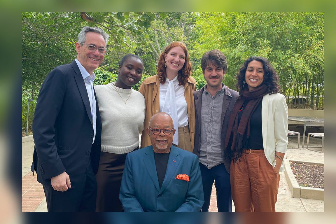 A group of six people — David Myers, Stephany Cartney, Celie Fischer, Mikey Aboutboul, and Felicia Graham — smile together outdoors in a lush garden setting with Henry Louis Gates Jr. seated in front.