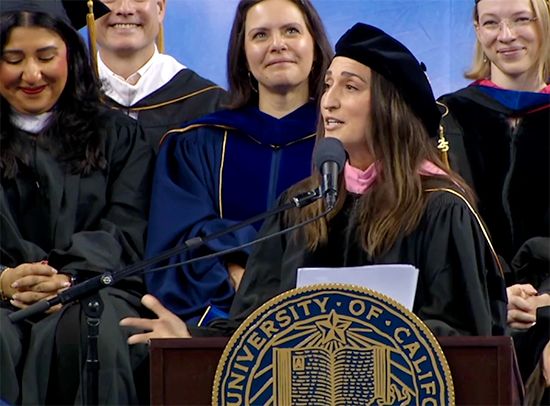 Sara Bareilles, in gown and dark beret, speaks at a podium bearing the UCLA seal