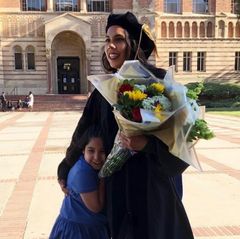 Melissa Ramirez smiles in doctoral regalia while holding a bouquet of flowers, as her niece Camila hugs her.