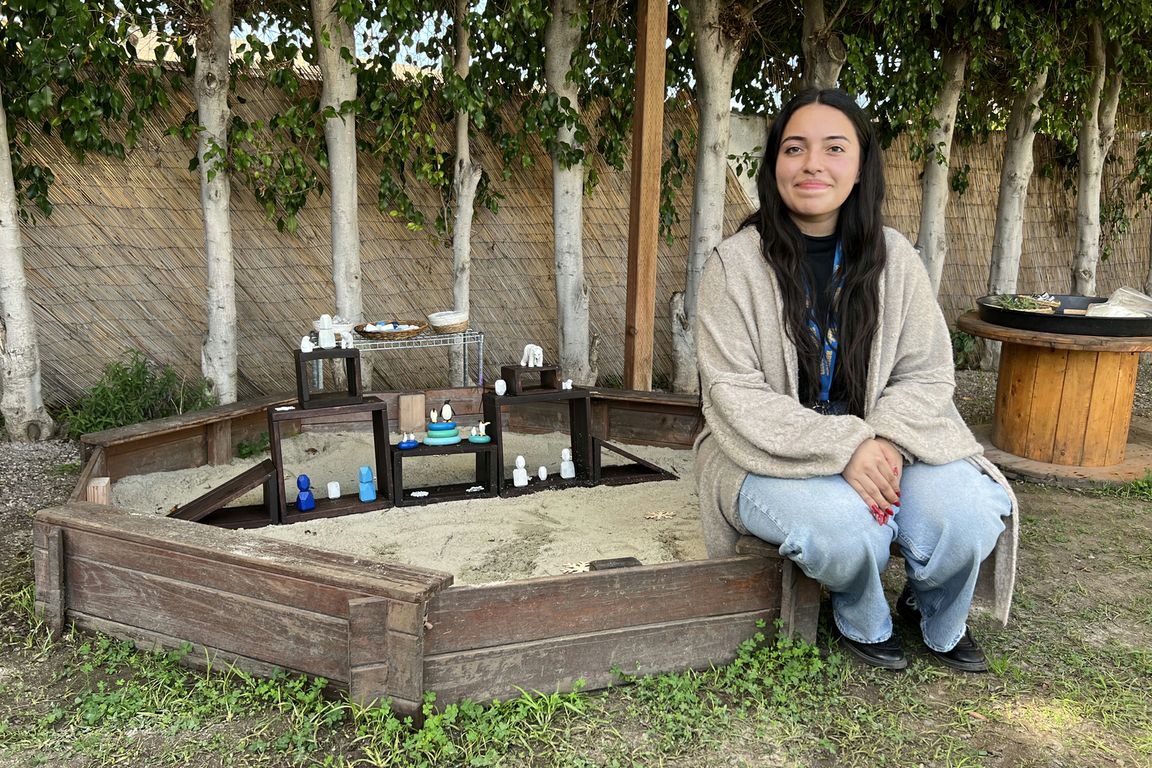 Stephanie Reynoso, a fourth-year UCLA education and social transformation student, sits beside a sand tray filled with repurposed figurines and objects used for play and art-making sessions.
