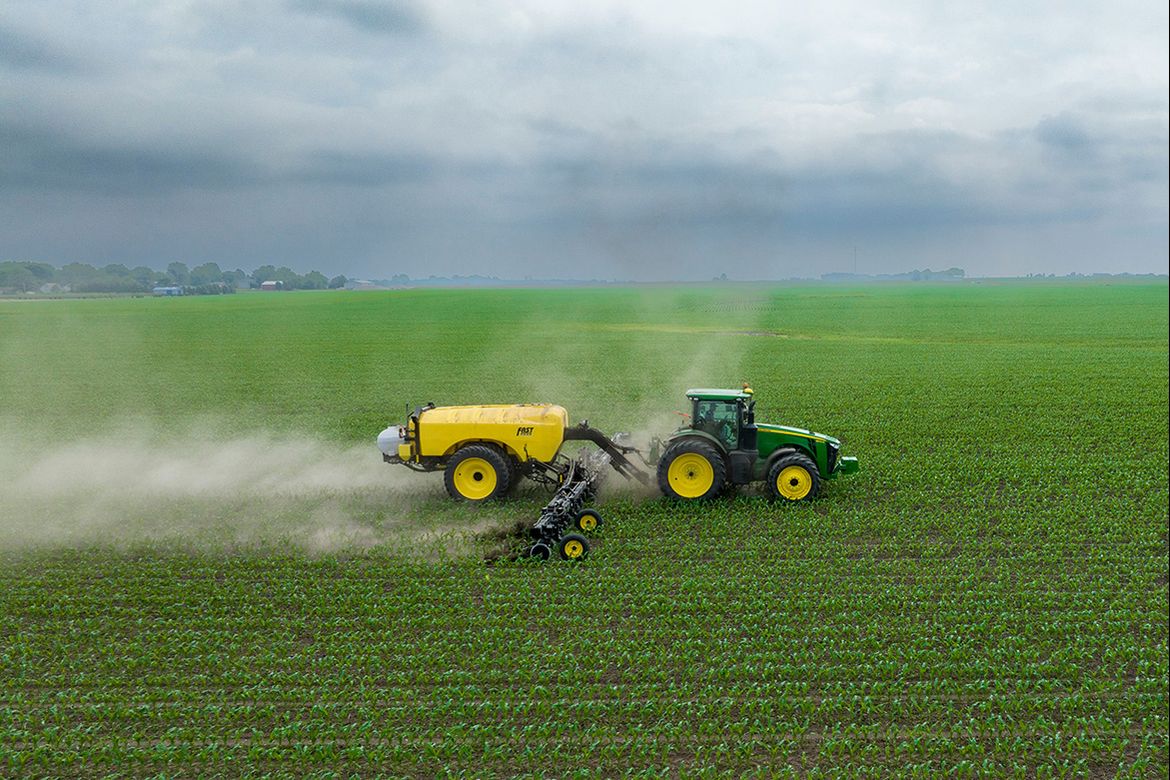 Green and yellow tractor spraying crops in a field