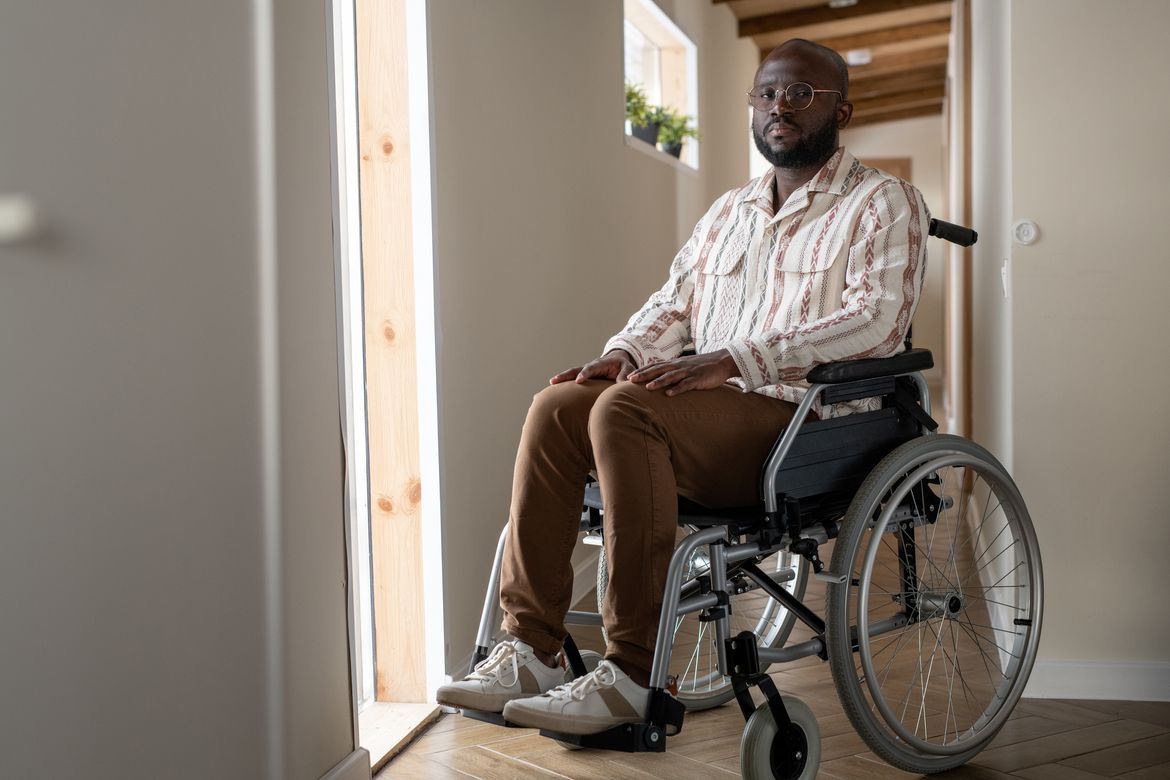 A man using a wheelchair sits in a sunlit hallway of a home.