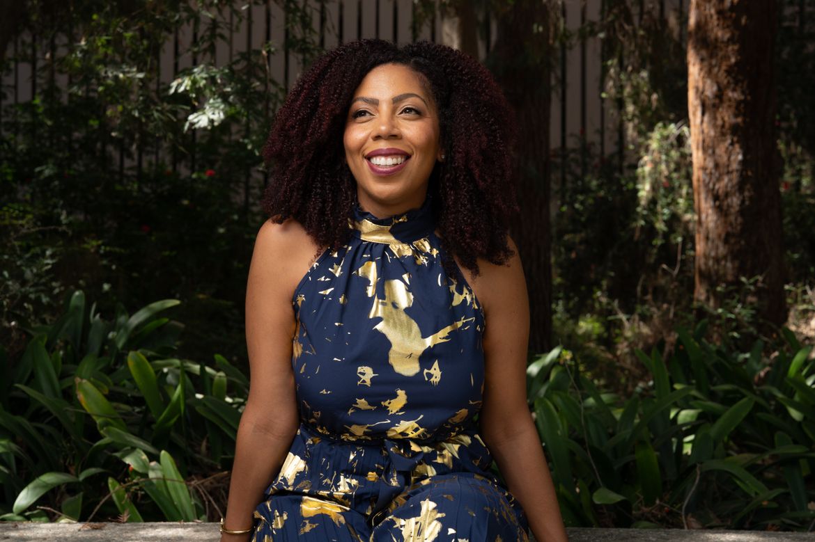A portrait of Jonli Tunstall smiling outdoors, seated in front of lush greenery.