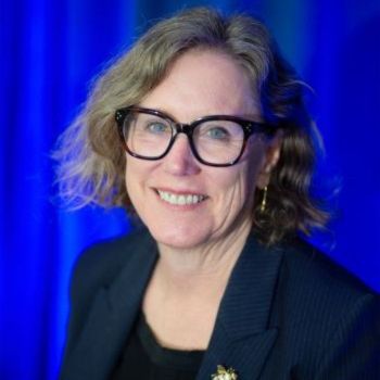 A headshot of Ann Carlson, who smiles against a blue background.