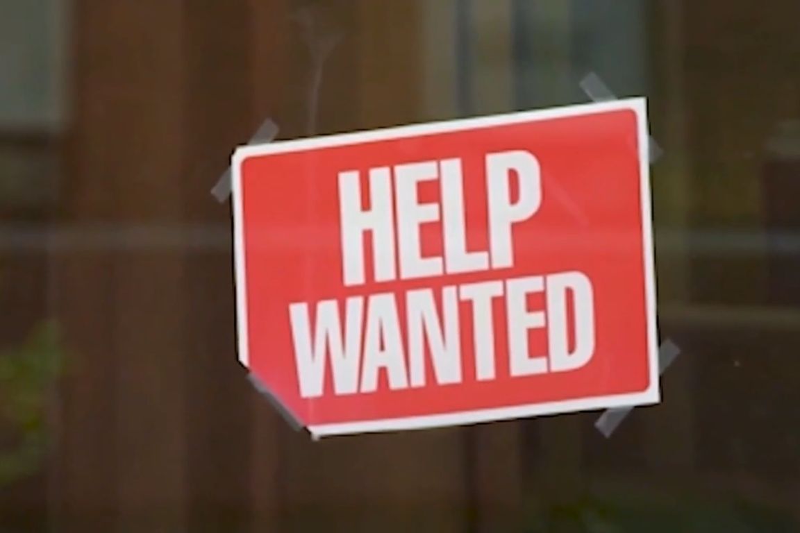  red "Help Wanted" sign is taped to a store window.
