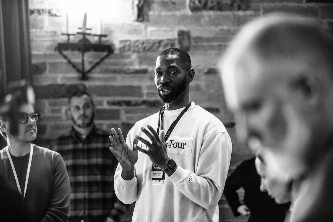Man in center gestures with hands in front of his chest as several people watch