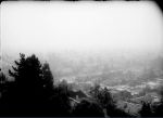 A black-and-white archival photograph from 1955 shows the Los Angeles skyline obscured by a thick layer of smog