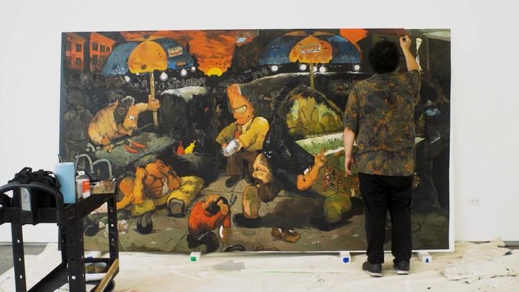 Iraqi visual artist Ali Eyal works on his large-scale painting "And Look Where I Went," featured in the Hammer Museum at UCLA's "Made in L.A. 2025" biennale, which depicts a vivid street scene with figures gathered beneath food vendor umbrellas against a fiery orange sky.