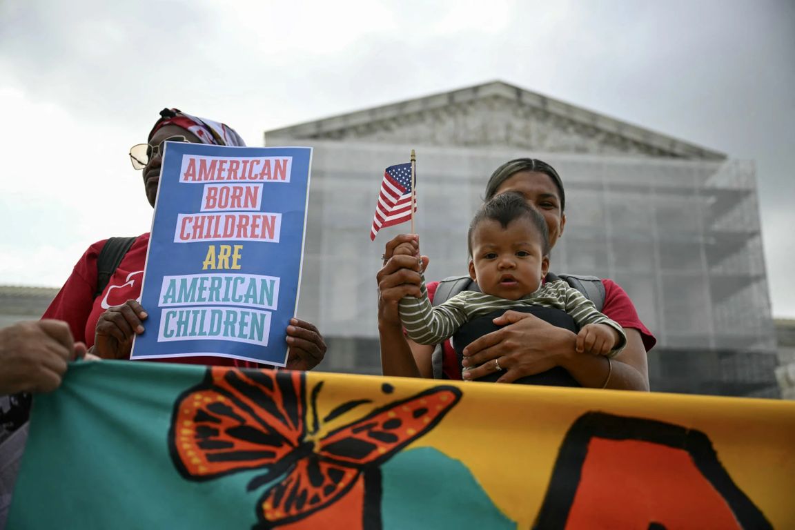 Demonstrators outside the U.S. Supreme Court hold a sign reading "American Born Children Are American Children" and a small American flag, with an infant in a carrier, during a rally supporting birthright citizenship.