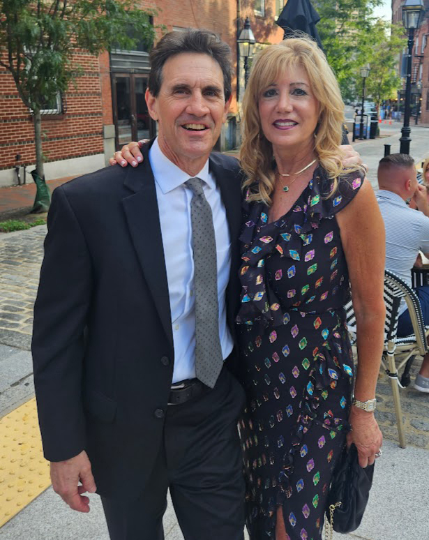Man with black suit and gray tie standing next to woman wearing patterned black sleeveless dress