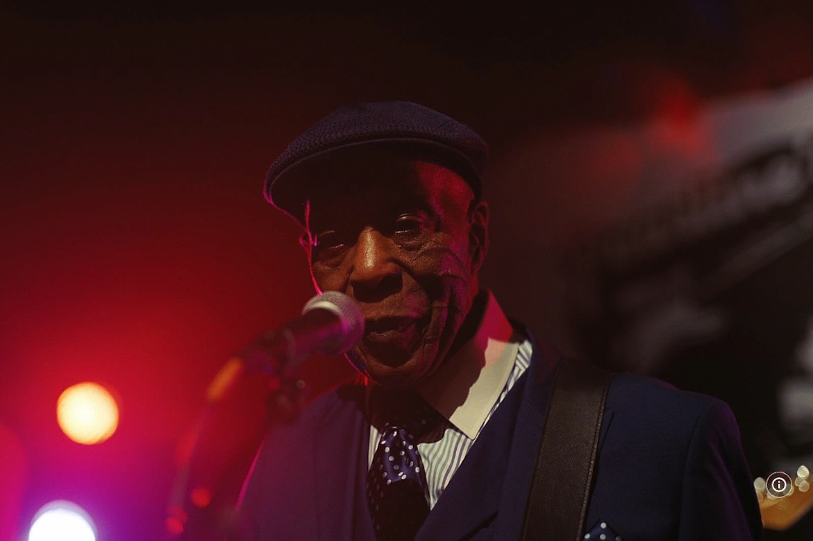 Still from "Sinners": Blues legend Buddy Guy sings into microphone