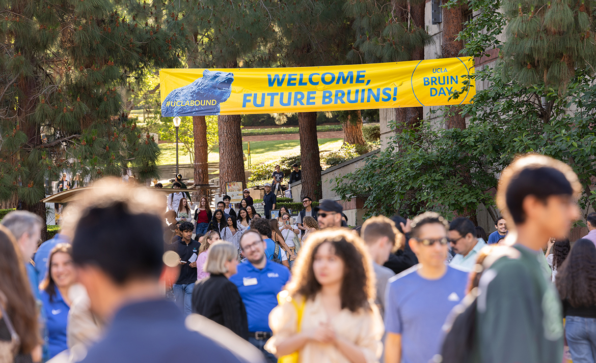 A large crowd of prospective students and families walks beneath a yellow banner reading "Welcome, Future Bruins!" with the UCLA Bruin Day logo and the hashtag #UCLABound. 