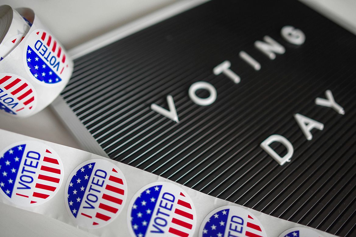 A black letter board displaying the words "Voting Day" is surrounded by rolls of circular red, white, and blue "I Voted" stickers.