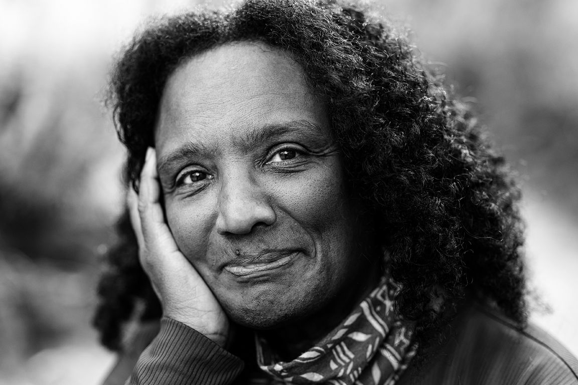 Black-and-white portrait of Harryette Mullen, UCLA professor of English, resting her cheek in her hand and smiling.
