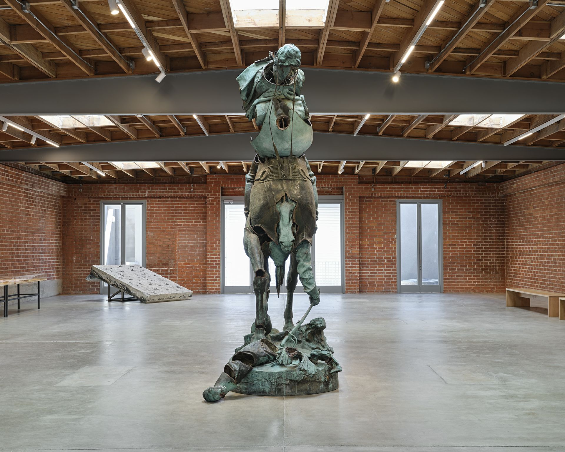 "Unmanned Drone," a towering bronze-patinated sculpture by Kara Walker depicting a rearing horse and rider, installed in a spacious brick-walled gallery.
