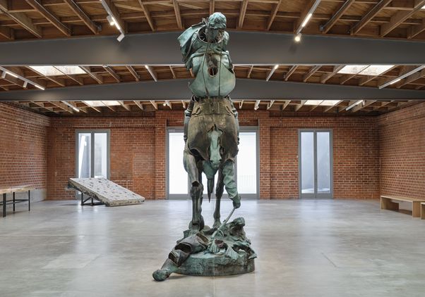 "Unmanned Drone," a towering bronze-patinated sculpture by Kara Walker depicting a rearing horse and rider, installed in a spacious brick-walled gallery.