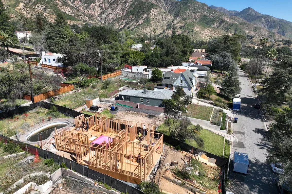 Aerial view of a home being rebuilt in Altadena, with wooden framing under construction surrounded by neighboring houses and tree-covered hills in the background. LA Times use only