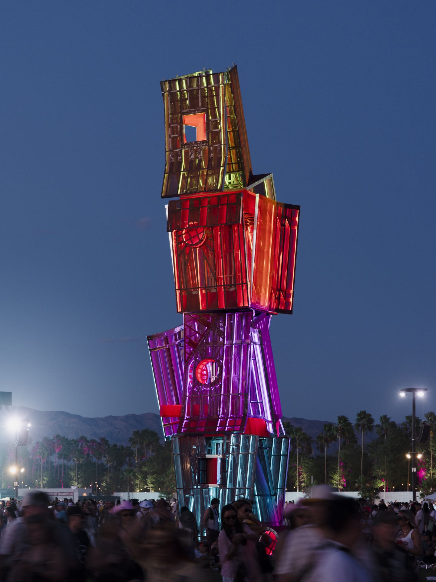 "Tower" of four large geometric boxes lit up at night in blue, purple, red and yellow
