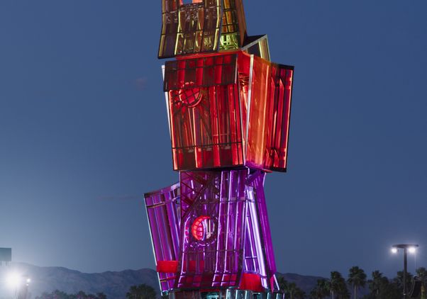 "Tower" of four large geometric boxes lit up at night in blue, purple, red and yellow