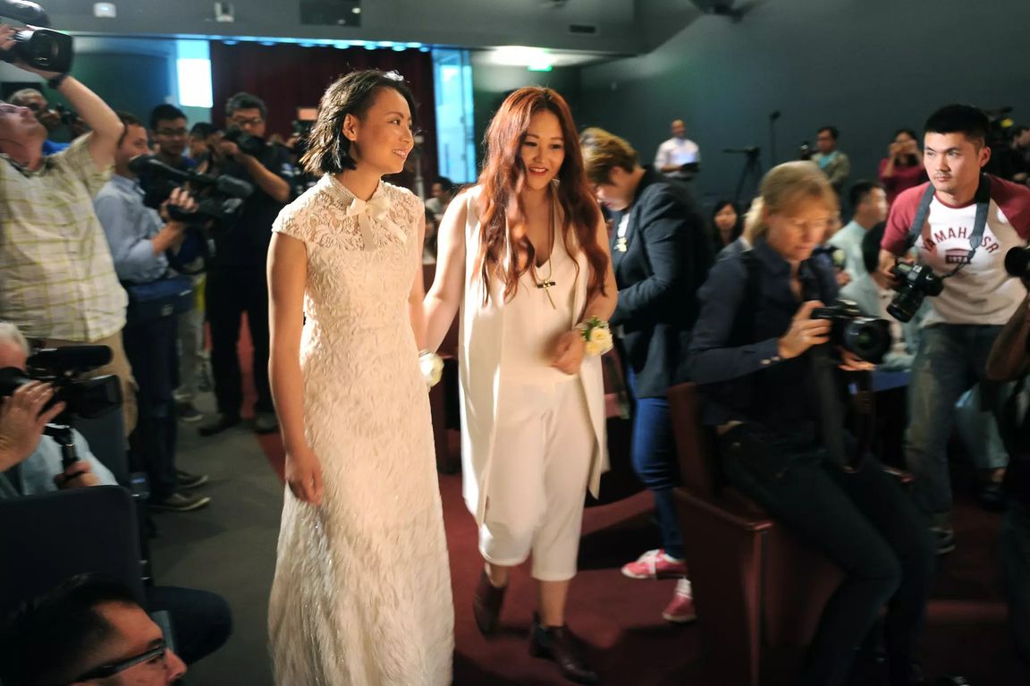 Two women in white wedding attire walk together during their 2015 West Hollywood wedding ceremony, surrounded by photographers and guests. (for LAT use only) 