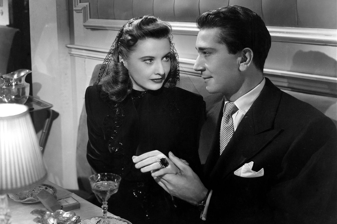 Black-and-white film still of a couple sitting next to each other at a restaurant holding hands