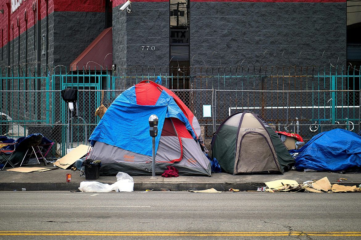 Group of tents on sidewalk with barbed wire fence behind