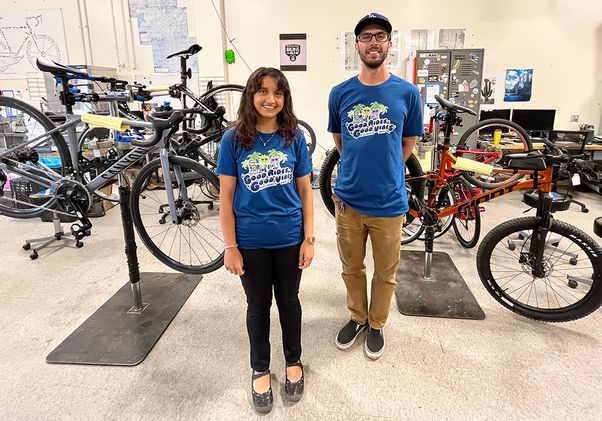 Sana Ahmed, left, in blue T-shirt and black pants, and Martin Espinoza, in blue T-shirt and brown pants, standing in a room with bicycles