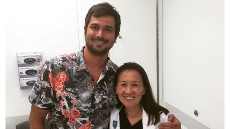 Dr. Linda Liau and patient Jamil Newirth stand together smiling in a clinical exam room.