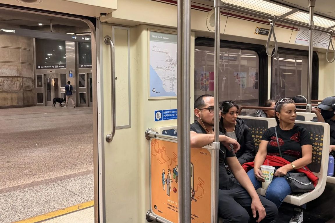 Passengers sit inside an L.A. Metro train car as the doors open at an underground station platform.